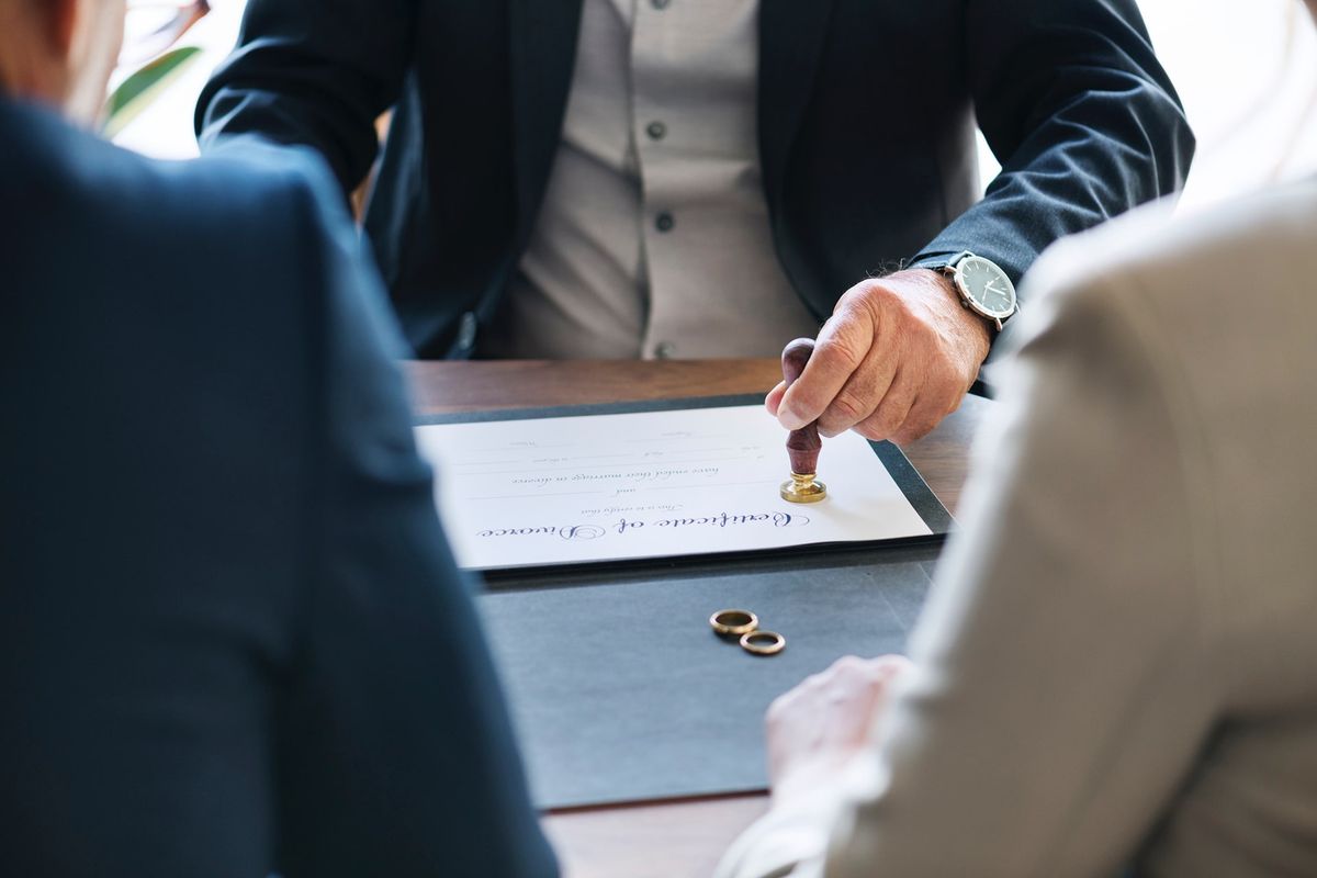 Hand stamping a divorce certificate beside wedding rings